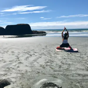 A woman in a yoga pose on a beach surrounded by beautiful scenery.