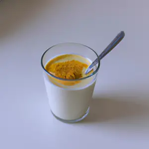 A glass of milk with a spoon of turmeric powder in it.