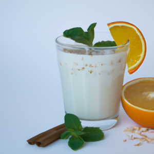 A glass of oat milk with a slice of orange, a sprig of mint, and a sprinkle of cinnamon.