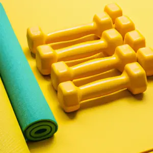 A bright yellow yoga mat with a stack of colorful dumbbells.